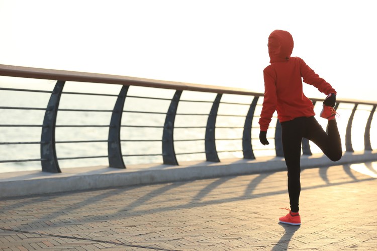 Young female runner stretching her legs on sunrise seaside